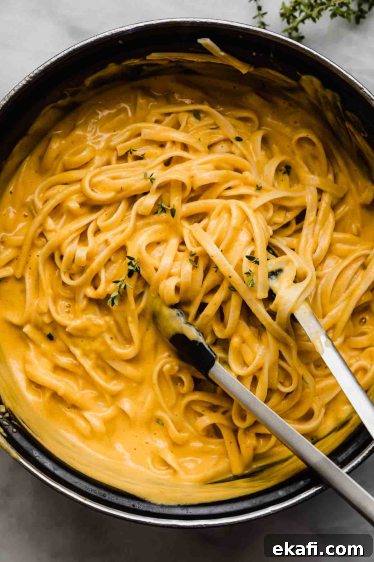 Αλφρέντο Γλυκοκολοκύθας 2 Κρεμώδες Butternut Squash Alfredo σε μαύρη κατσαρόλα με τσιμπίδες κουζίνας να ανακατεύουν τα ζυμαρικά.