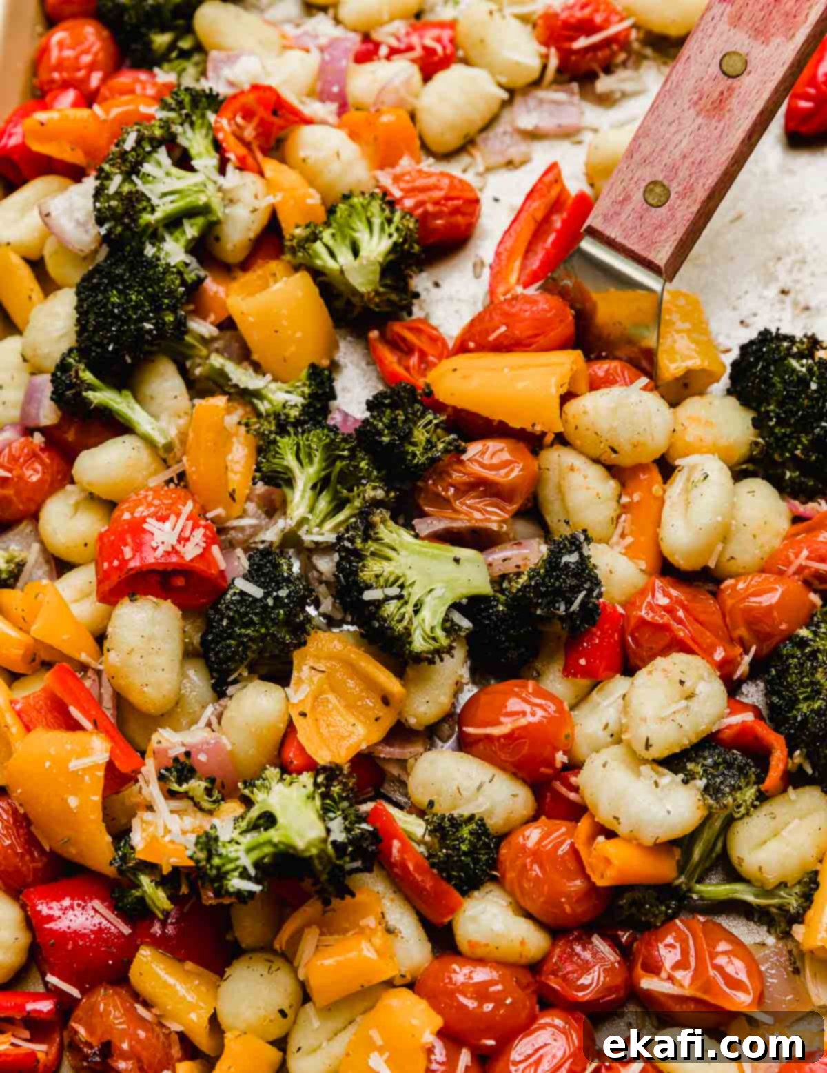Νιόκι και Λαχανικά: Όλα σε Ένα Ταψί 7 Ψητά gnocchi και λαχανικά στο ταψί με μια μεταλλική σπάτουλα που κρατά τα λαχανικά.