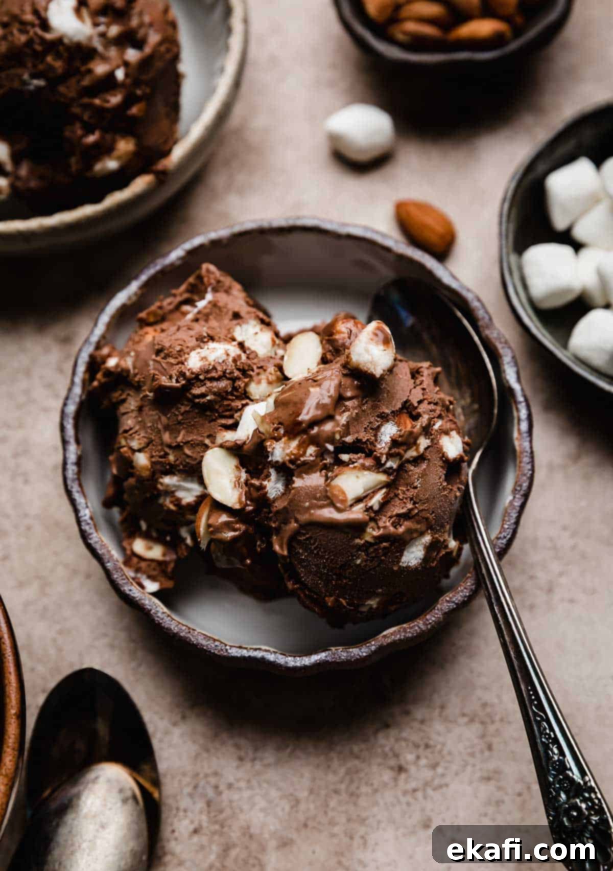 Easy Homemade Rocky Road Ice Cream 9 Two scoops of Rocky Road Ice Cream in a black rimmed bowl on a light brown textured background.
