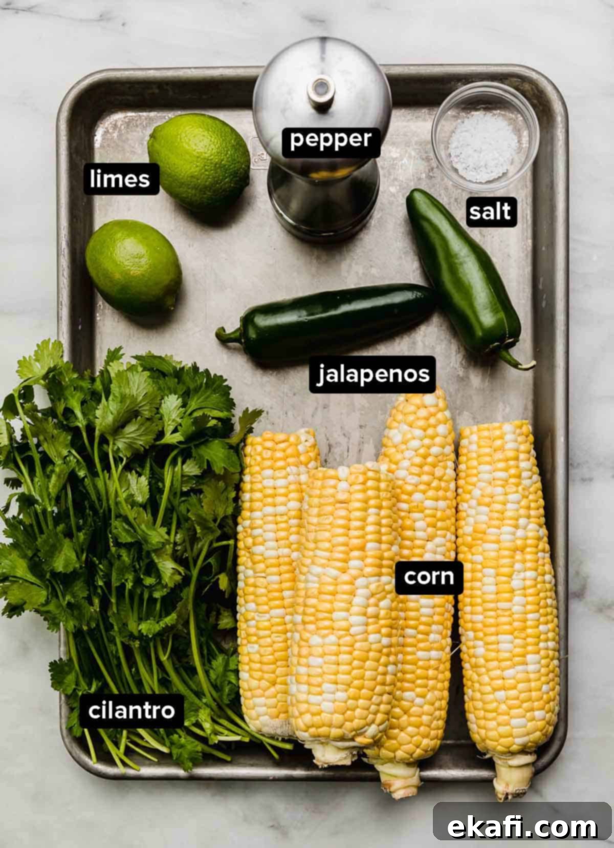 Summer Corn Salsa 3 Corn salsa recipe ingredients on a silver baking sheet: fresh corn on the cob, cilantro, jalapeños, limes, and salt and pepper.