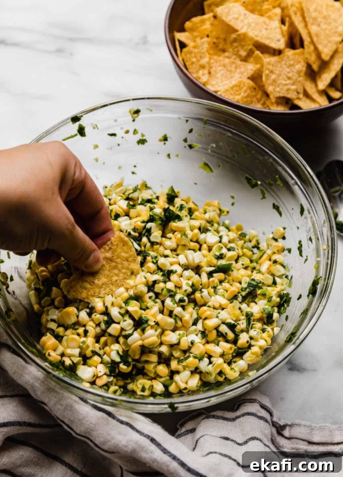 Summer Corn Salsa 5 A hand holding a tortilla chip, scooping up some corn salsa with jalapeño and cilantro.