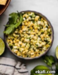 Summer Corn Salsa 6 Overhead photo of corn salsa made with raw corn in a black bowl on a white background with fresh limes surrounding the bowl.