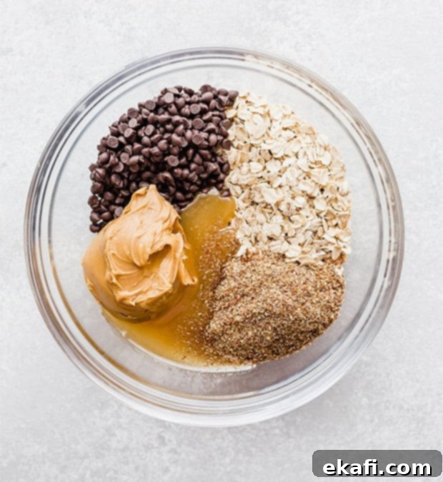 Effortless Power Bites 4 A glass bowl with oats, chocolate chips, peanut butter, flax seed, honey, and vanilla; prepping to make no-bake energy bites.