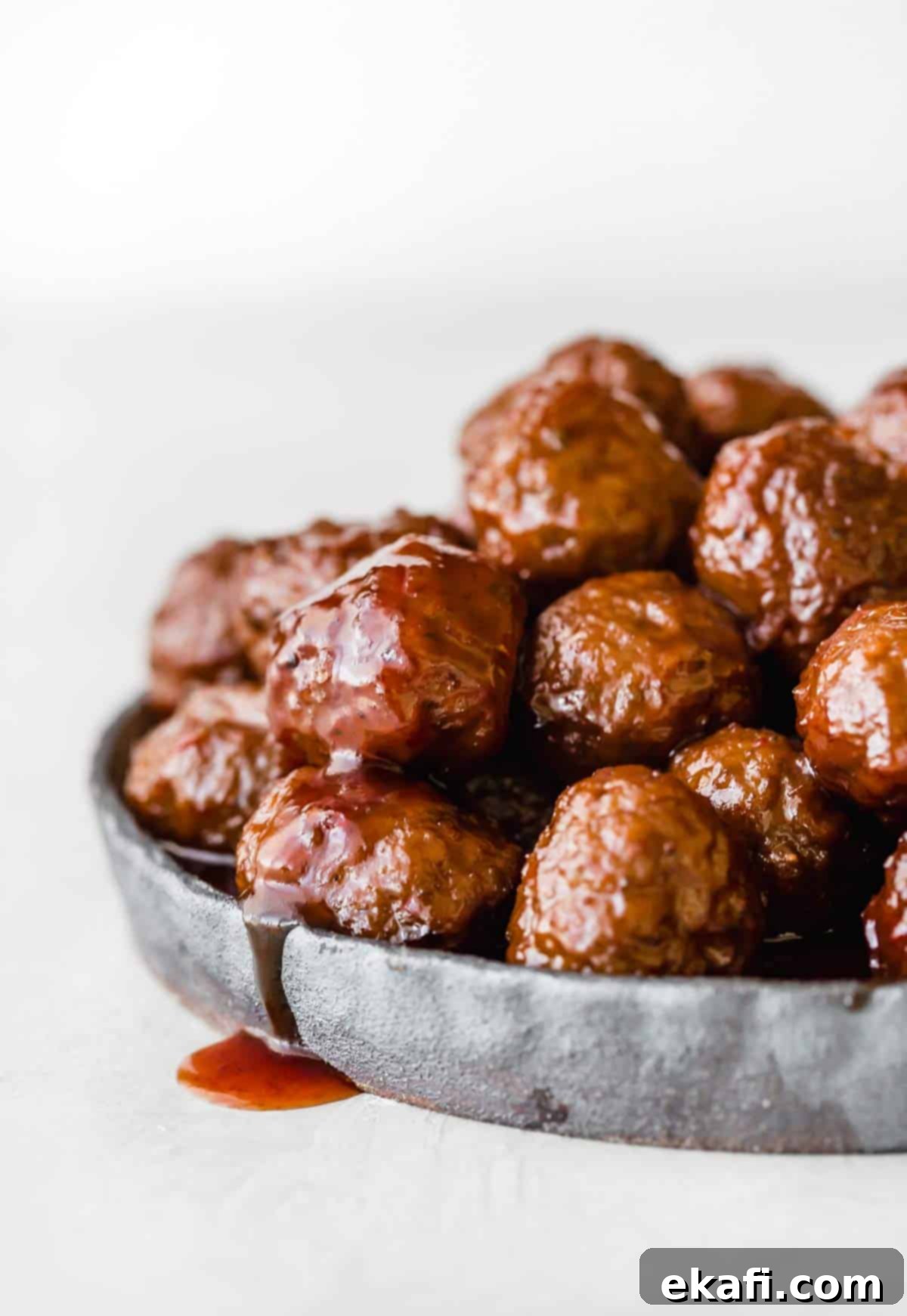 Sweet and Tangy Slow Cooker Meatballs 2 Grape Jelly Meatballs on a black plate against a white background, garnished with parsley.