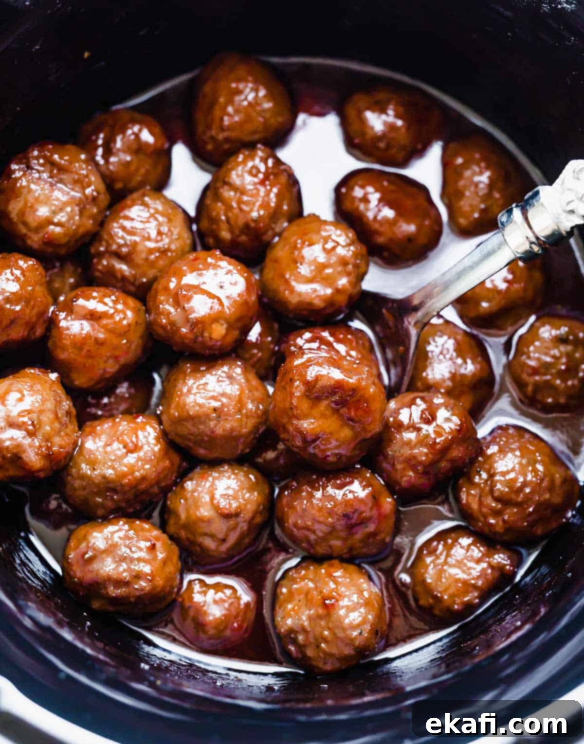 Sweet and Tangy Slow Cooker Meatballs 6 Grape Jelly Meatballs simmering in a round black crock pot.