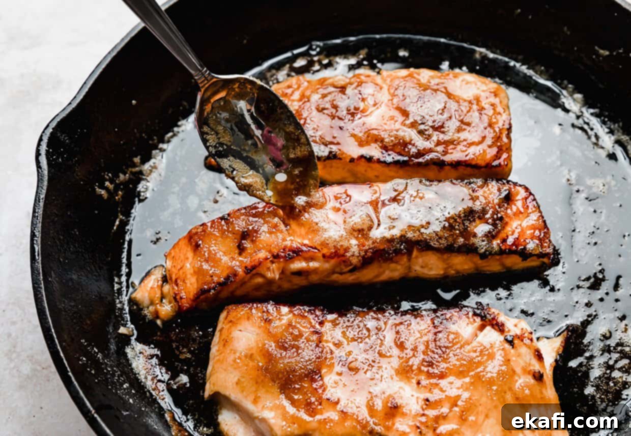 Caramelized Brown Sugar Salmon 6 A spoon meticulously drizzles glistening brown sugar glaze over a perfectly seared salmon fillet resting in a black skillet, emphasizing the sweet crust.