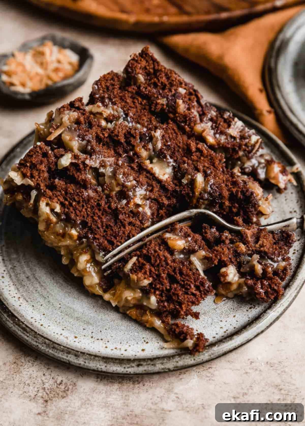 Decadent German Chocolate Creation 8 A slice of Traditional German Chocolate Cake made with sour cream, on a gray plate with a fork cutting into the cake.