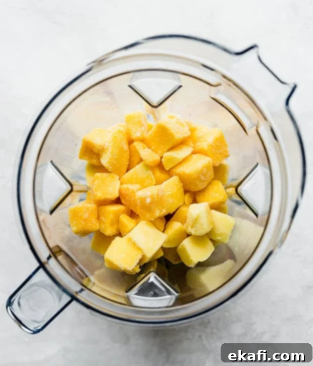 Tropical Mango Freeze 4 A blender full of vibrant yellow frozen mango chunks, partially blended, in preparation for making mango sorbet. The blades are visible, and the texture is still chunky.