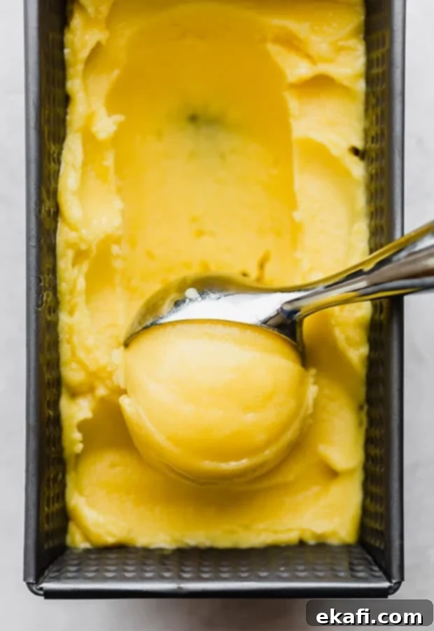 Tropical Mango Freeze 7 A scoop of creamy mango sorbet being lifted from a bowl with an ice cream scoop, showcasing its smooth and soft texture. The sorbet is a vibrant orange color.
