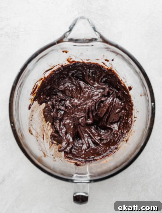 Fudgy Brownie Cookies 5 A close-up shot of rich, dark brownie cookie batter in a clear glass bowl, showcasing its thick consistency and the generous inclusion of chocolate chips, ready for scooping.