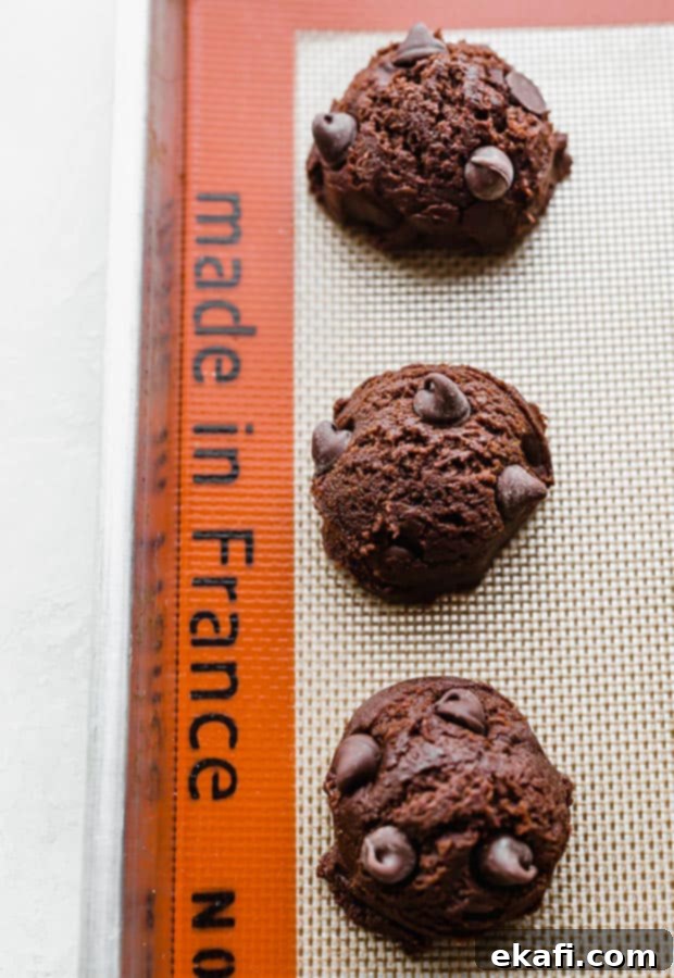 Fudgy Brownie Cookies 6 Raw brownie cookie dough balls, perfectly scooped and spaced, arranged on a baking sheet lined with parchment paper, awaiting their transformation in the oven.