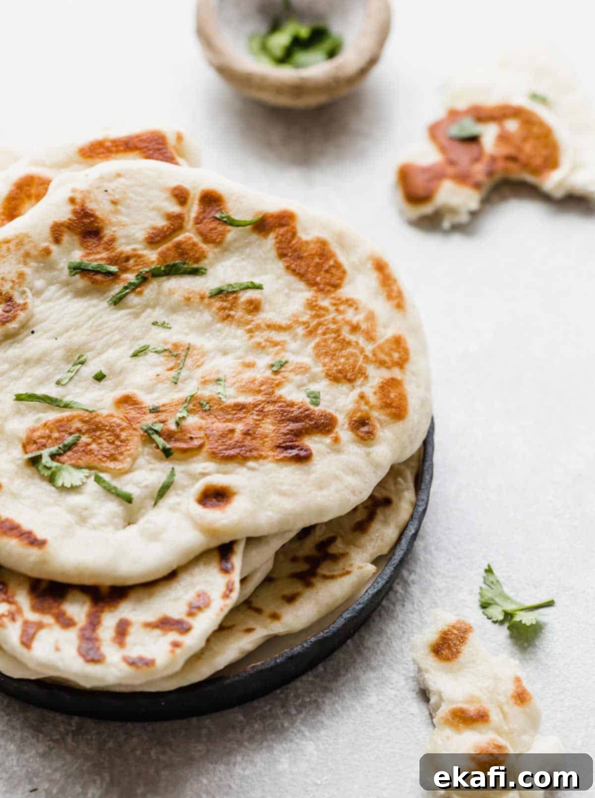 Pillowy Greek Yogurt Naan 2 Freshly made Greek Yogurt Naan Bread on a black plate, garnished with chopped cilantro, showcasing its tender and chewy texture.