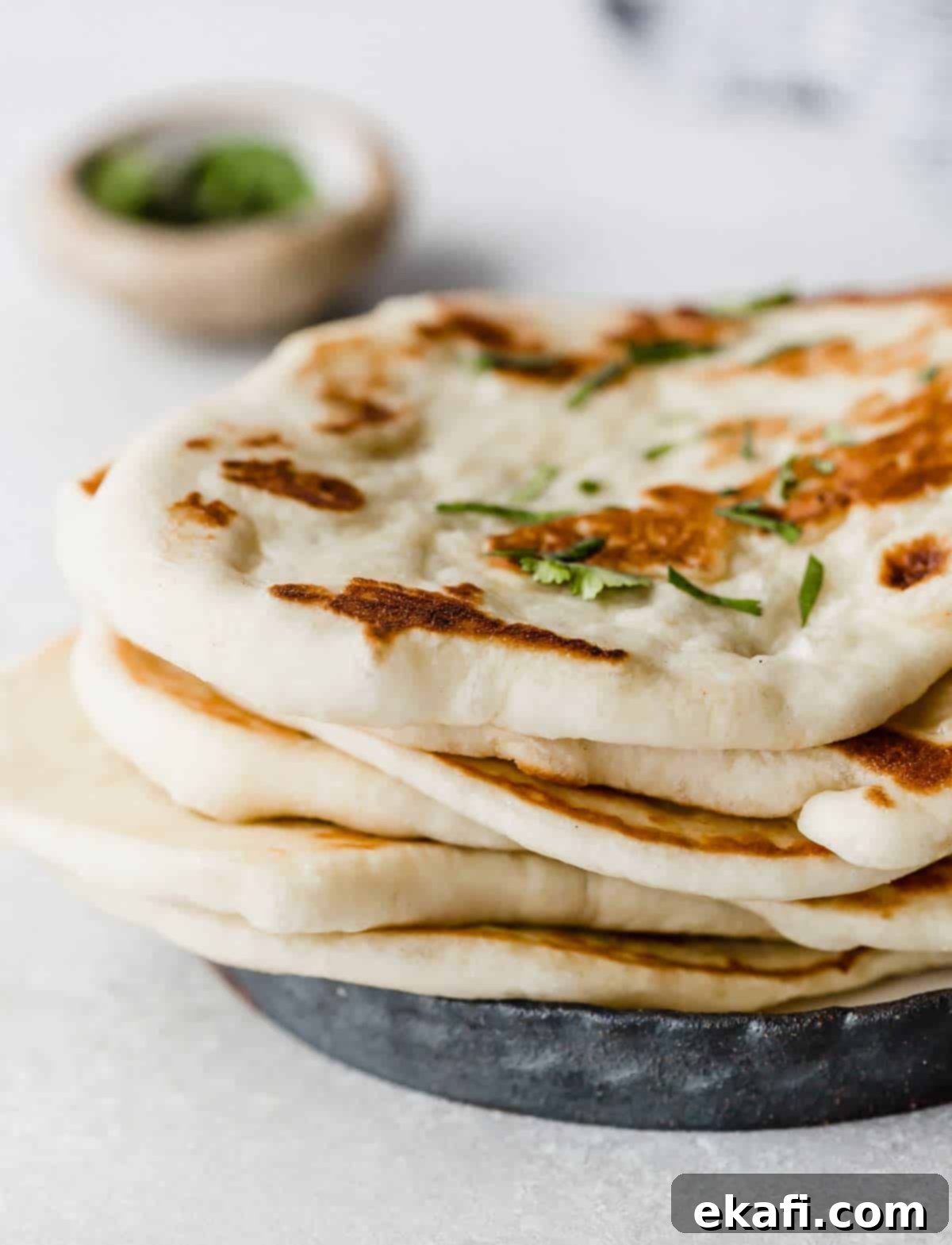 Pillowy Greek Yogurt Naan 6 A stack of Greek Yogurt Naan Bread on a black plate, garnished with fresh cilantro.