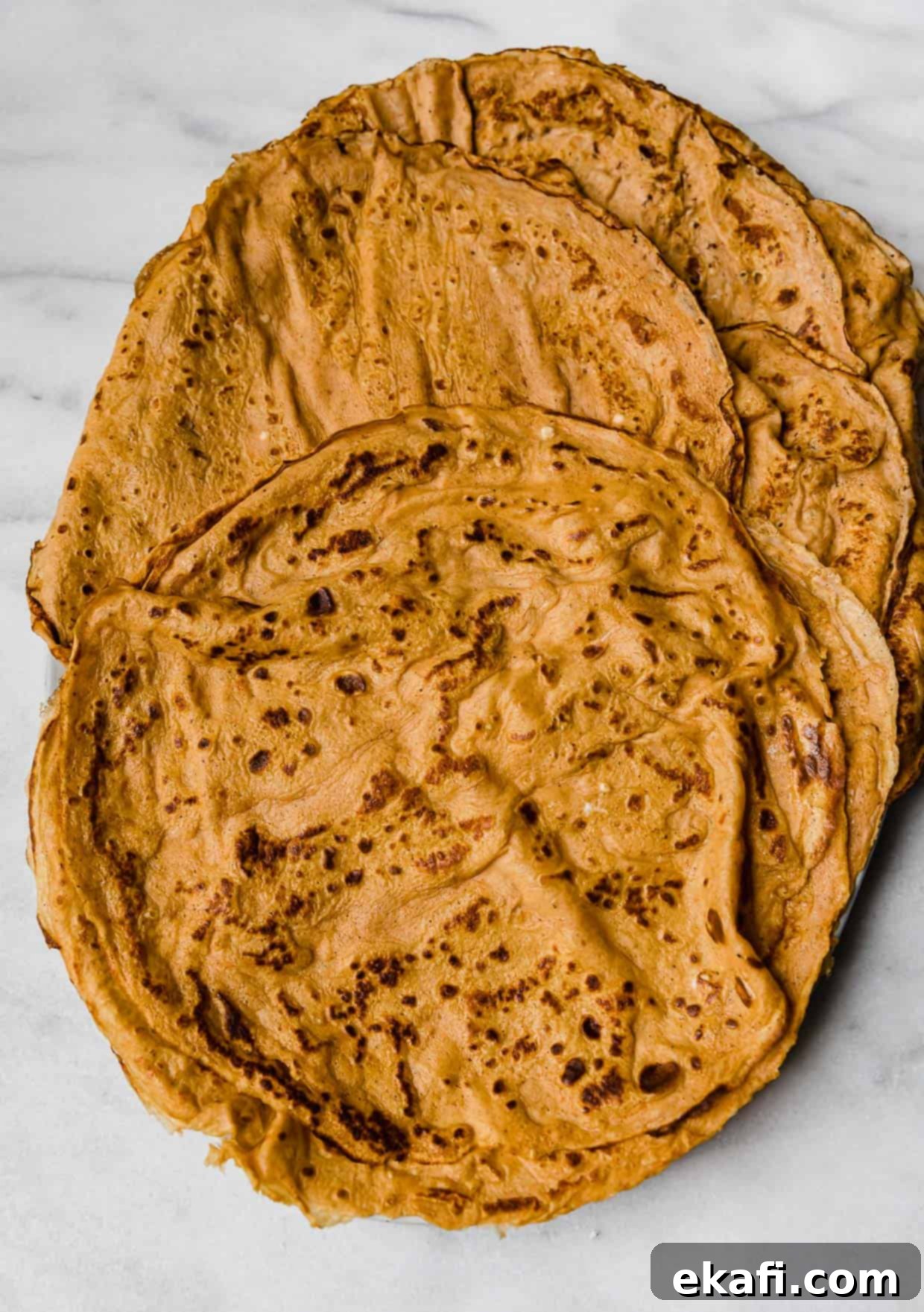 Autumn Pumpkin Crepes 6 A stack of orange pumpkin crepes on a marble table.