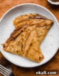 Autumn Pumpkin Crepes 8 Two Nutella filled pumpkin crepes on a white plate.
