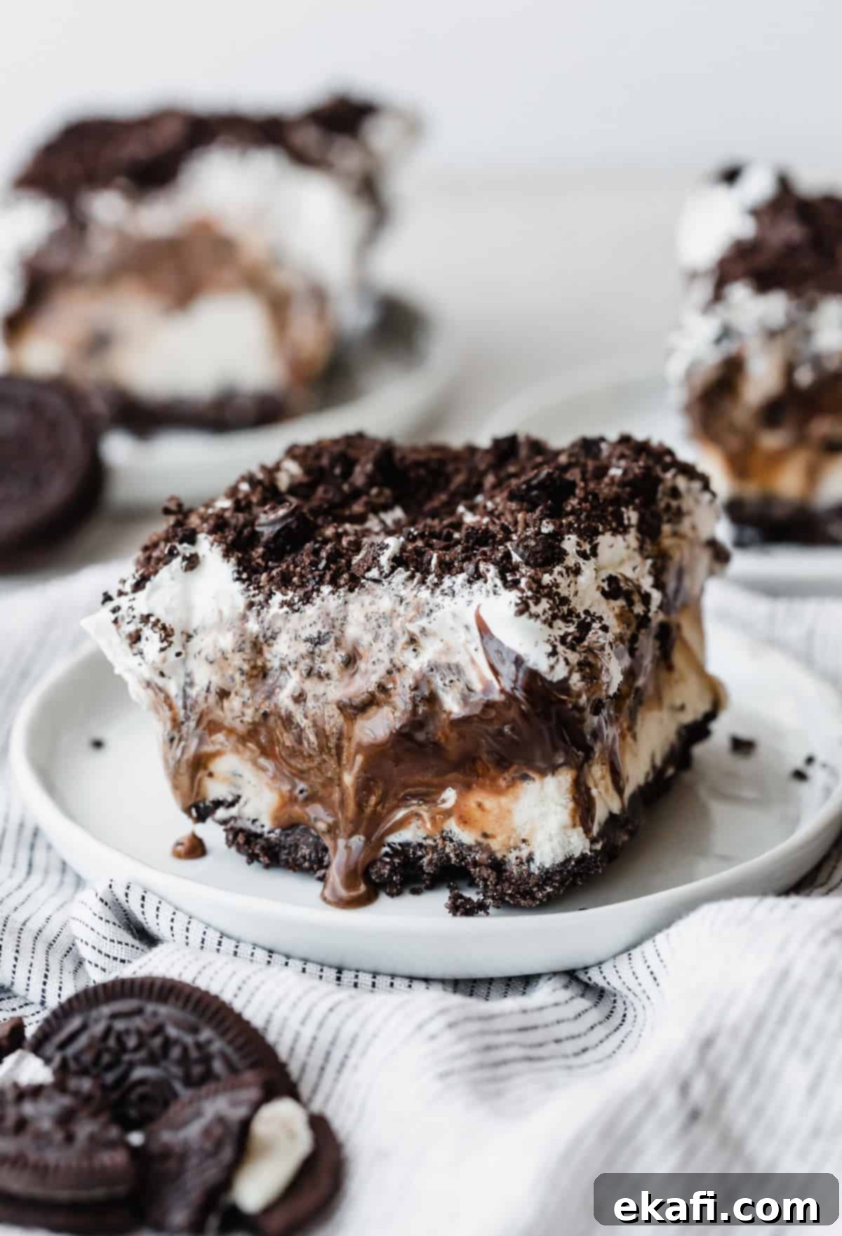 Frozen Oreo Indulgence 2 A perfectly square slice of Oreo Ice Cream Cake, showcasing distinct layers of crushed Oreos, creamy ice cream, hot fudge, and whipped topping, garnished with more crushed Oreos.