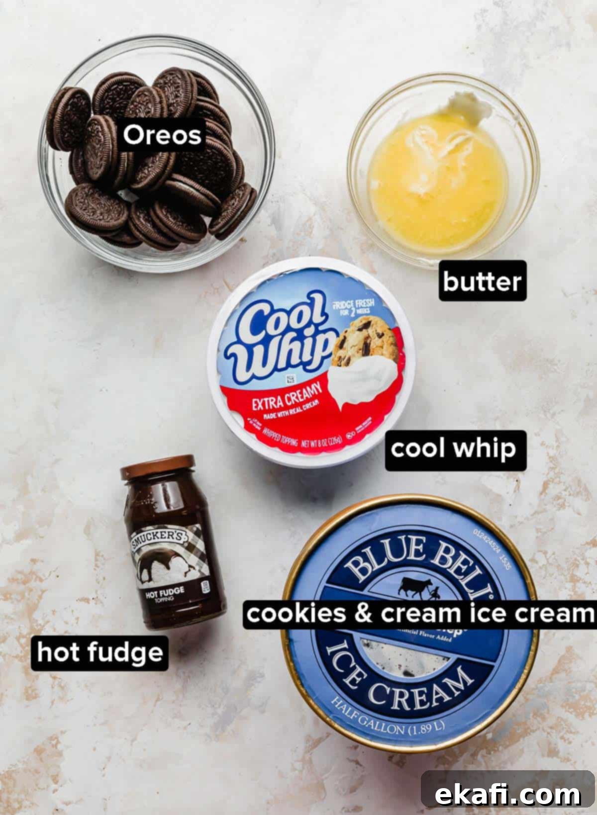 Frozen Oreo Indulgence 3 A collection of ingredients for Oreo Ice Cream Cake, including Oreos, melted butter, Cookies 'n Cream ice cream, Cool Whip, and hot fudge, neatly arranged in glass bowls.