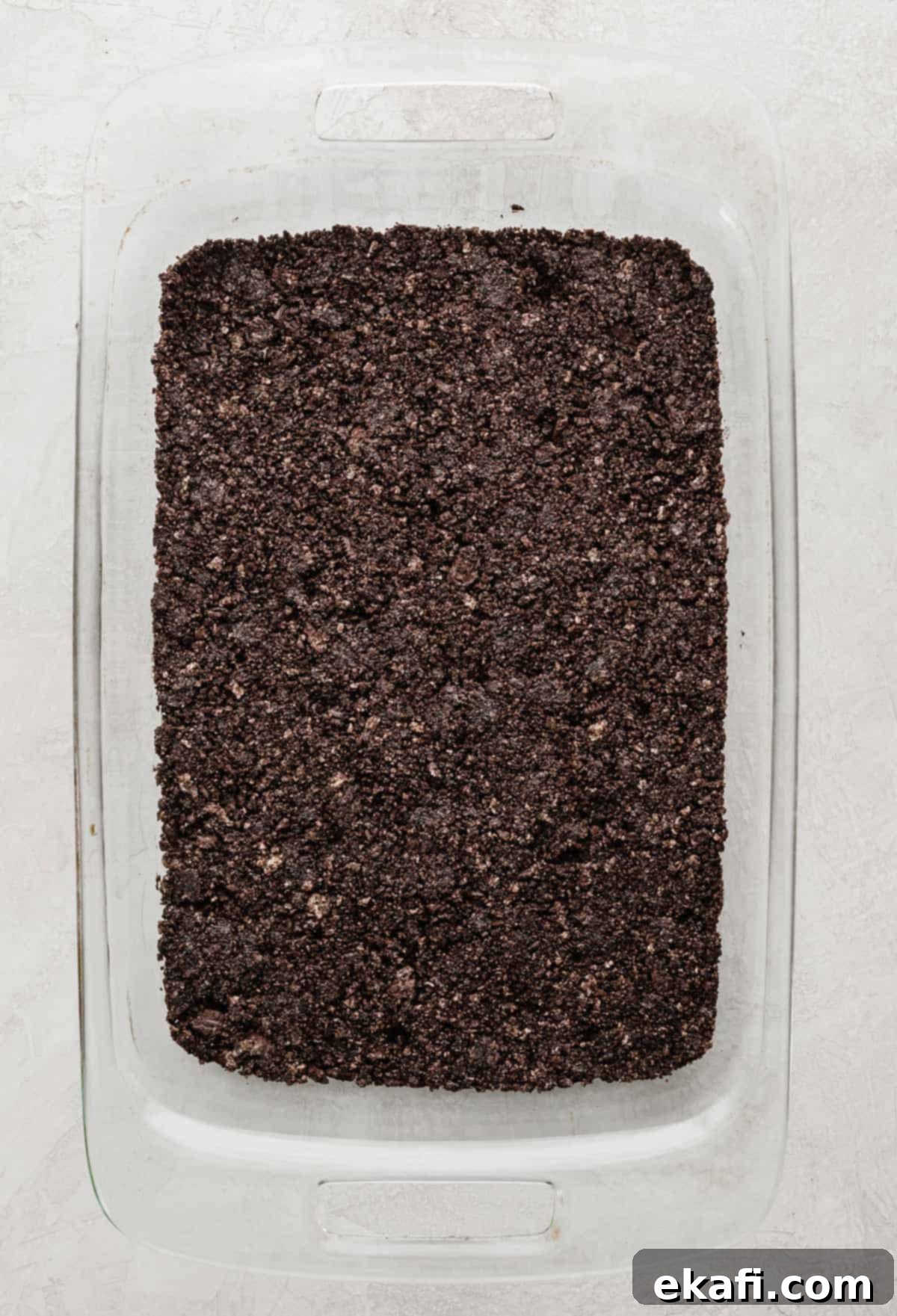 Frozen Oreo Indulgence 4 Crushed Oreo crust, perfectly pressed and covering the bottom of a rectangular glass baking dish, ready for the next layer of ice cream.