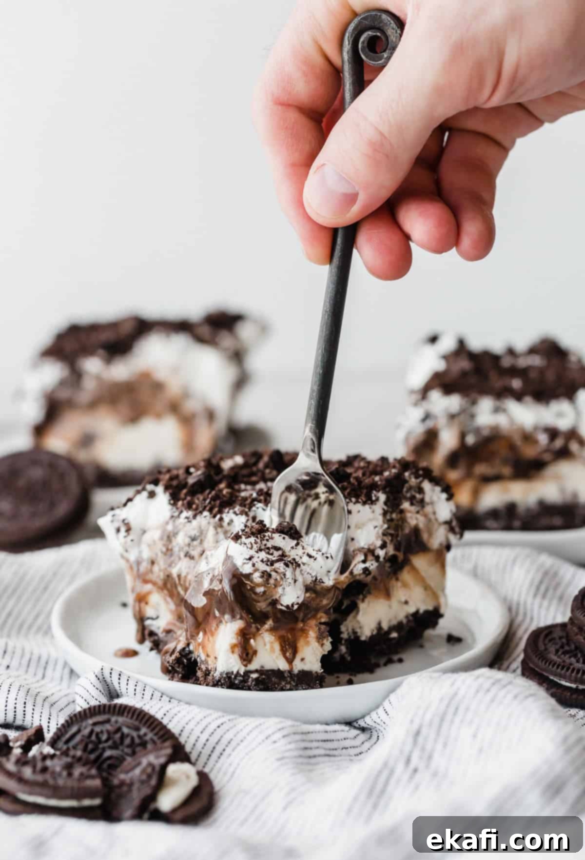 Frozen Oreo Indulgence 8 A hand holding a fork, poised to take a bite from a tempting slice of Oreo Ice Cream Cake, served on a white plate, highlighting the delicious layers.