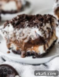 Frozen Oreo Indulgence 9 A perfectly cut slice of homemade Oreo Ice Cream Cake on a white plate, topped with a generous sprinkle of crushed Oreos, ready to be enjoyed.