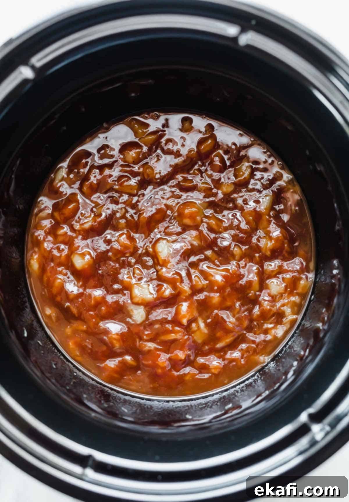 Sticky Pineapple BBQ Meatballs 4 A close-up shot of rich BBQ sauce and golden crushed pineapple mixing together in a black round crockpot, ready for the meatballs.
