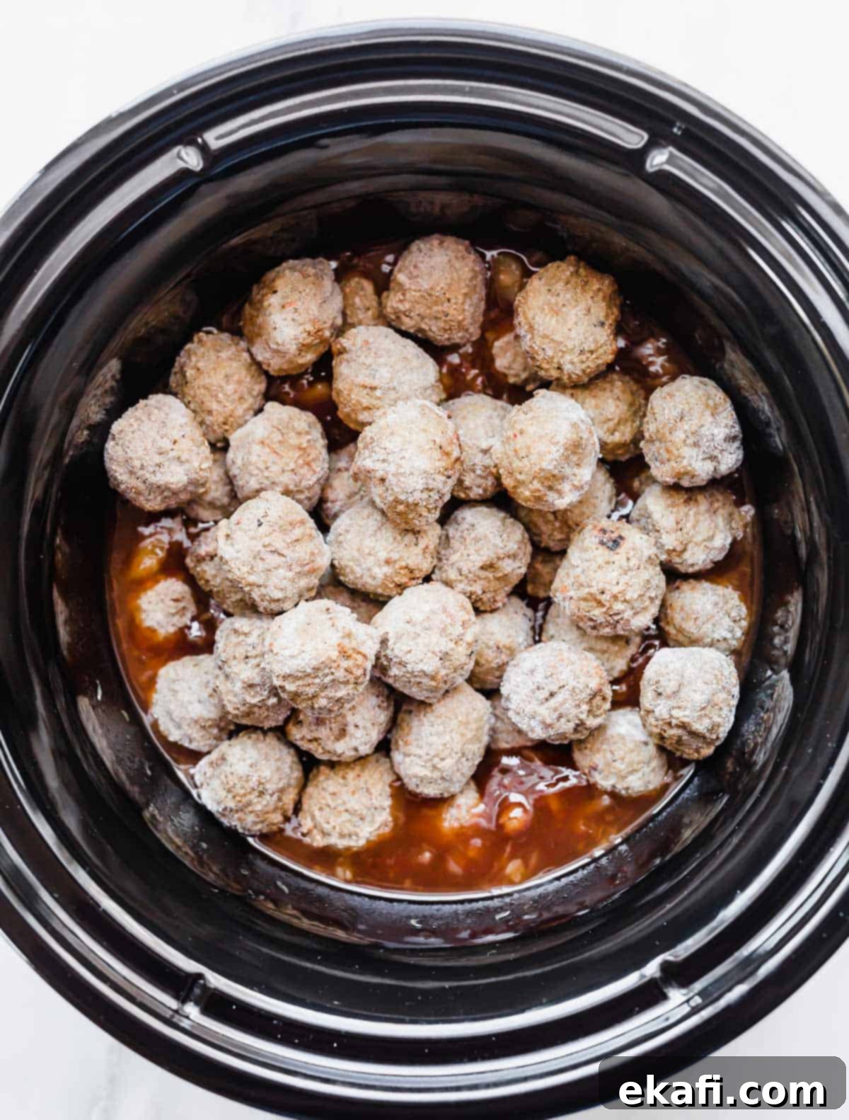 Sticky Pineapple BBQ Meatballs 5 Frozen meatballs are gently added to the black crockpot, resting on the vibrant mixture of BBQ sauce and crushed pineapple, ready to be stirred.