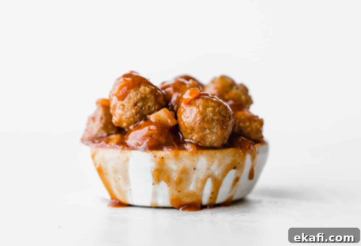 Sticky Pineapple BBQ Meatballs 7 A white bowl overflowing with glossy BBQ Pineapple Meatballs, with delicious sauce spilling over the side onto a clean white background.