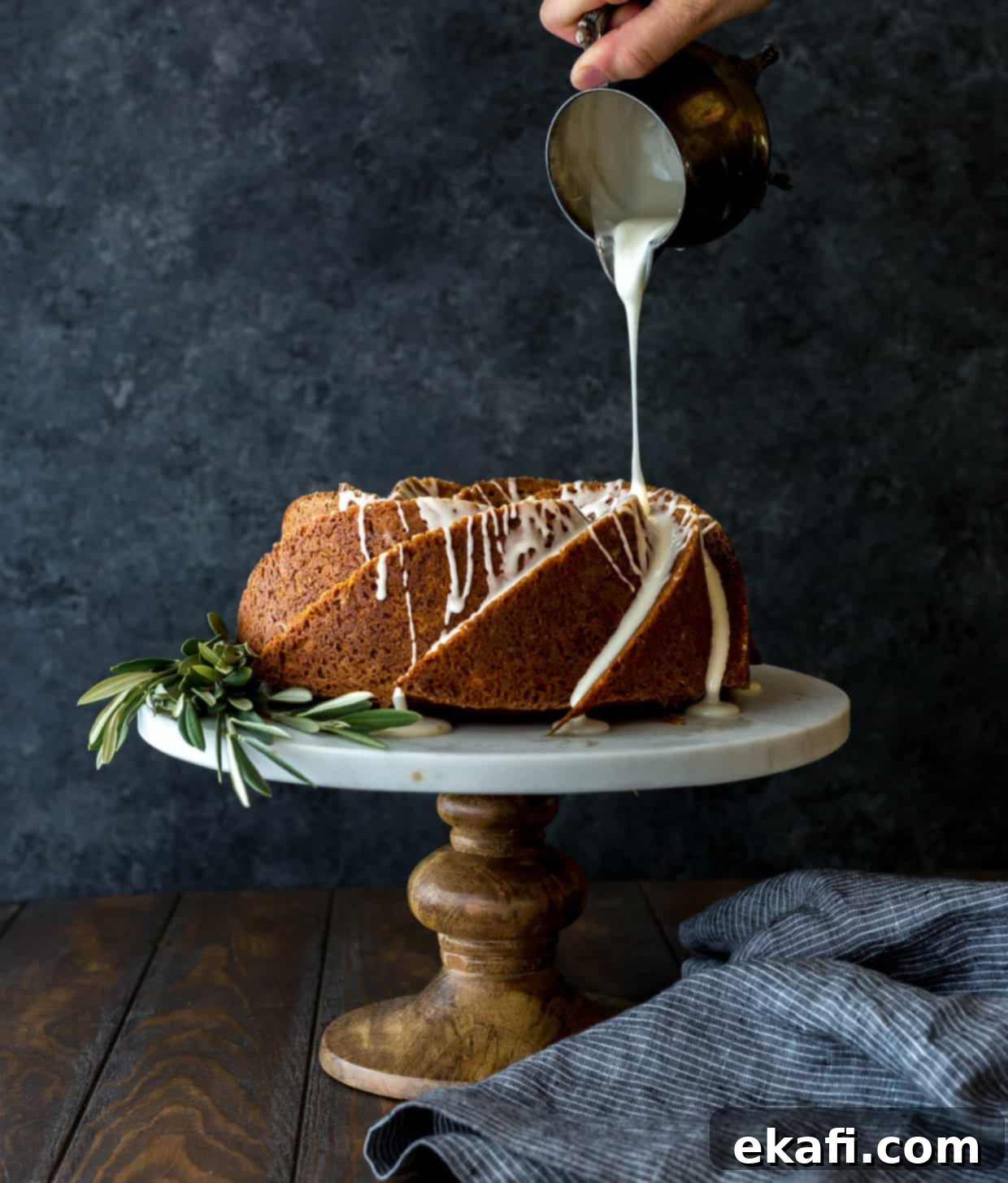 Spiced Gingerbread Bundt Delight 3 A beautifully decorated gingerbread bundt cake, presented on an elegant white cake stand with fresh olive branches as a festive decoration at its base, highlighting its intricate design.