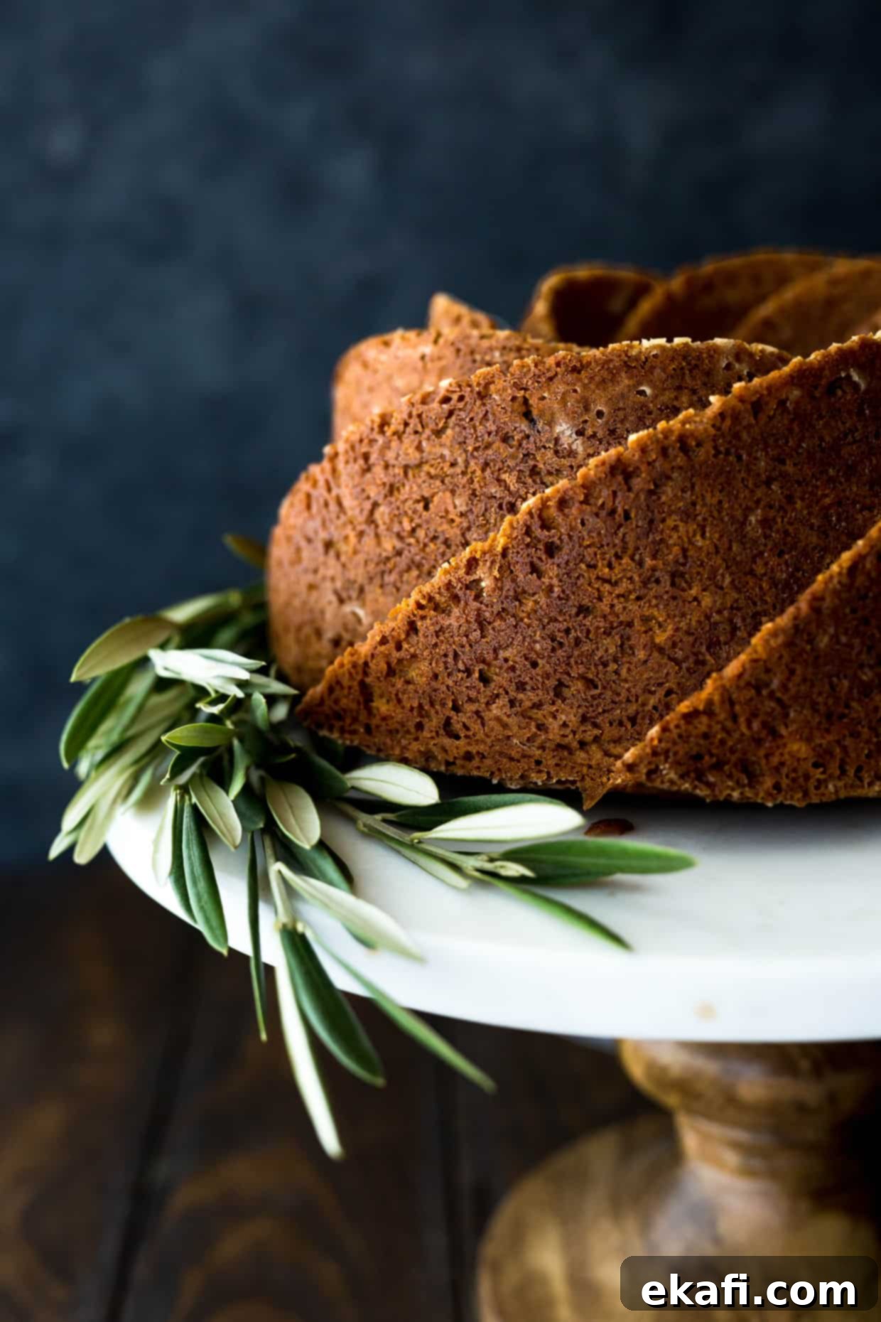 Spiced Gingerbread Bundt Delight 4 Close up shot of a spiral-patterned gingerbread bundt cake on a cake stand, adorned with olive branches at its base, showcasing its intricate design and golden-brown crust.