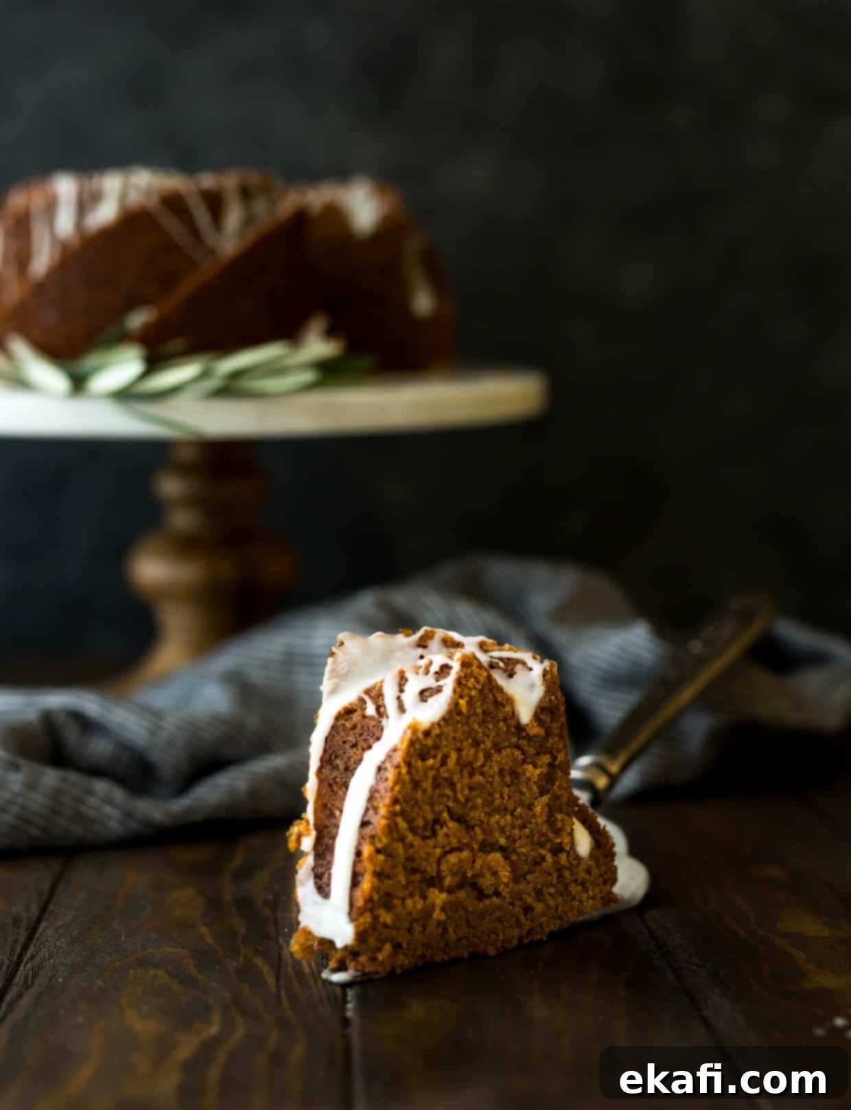 Spiced Gingerbread Bundt Delight 5 A perfectly sliced piece of gingerbread bundt cake in the foreground, showing its moist texture, with the remaining glazed bundt cake on a decorative cake stand in the background.