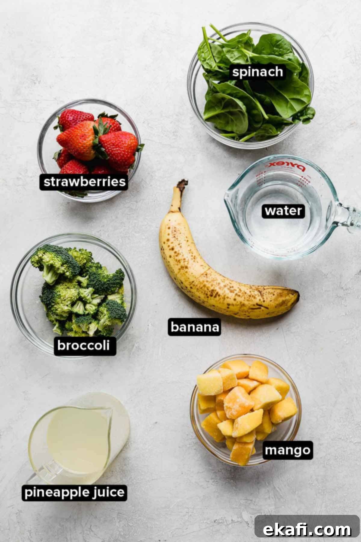 Green Power Smoothie 3 Broccoli Smoothie ingredients on a white background: strawberries, spinach, broccoli, banana, mango, pineapple juice, and water.