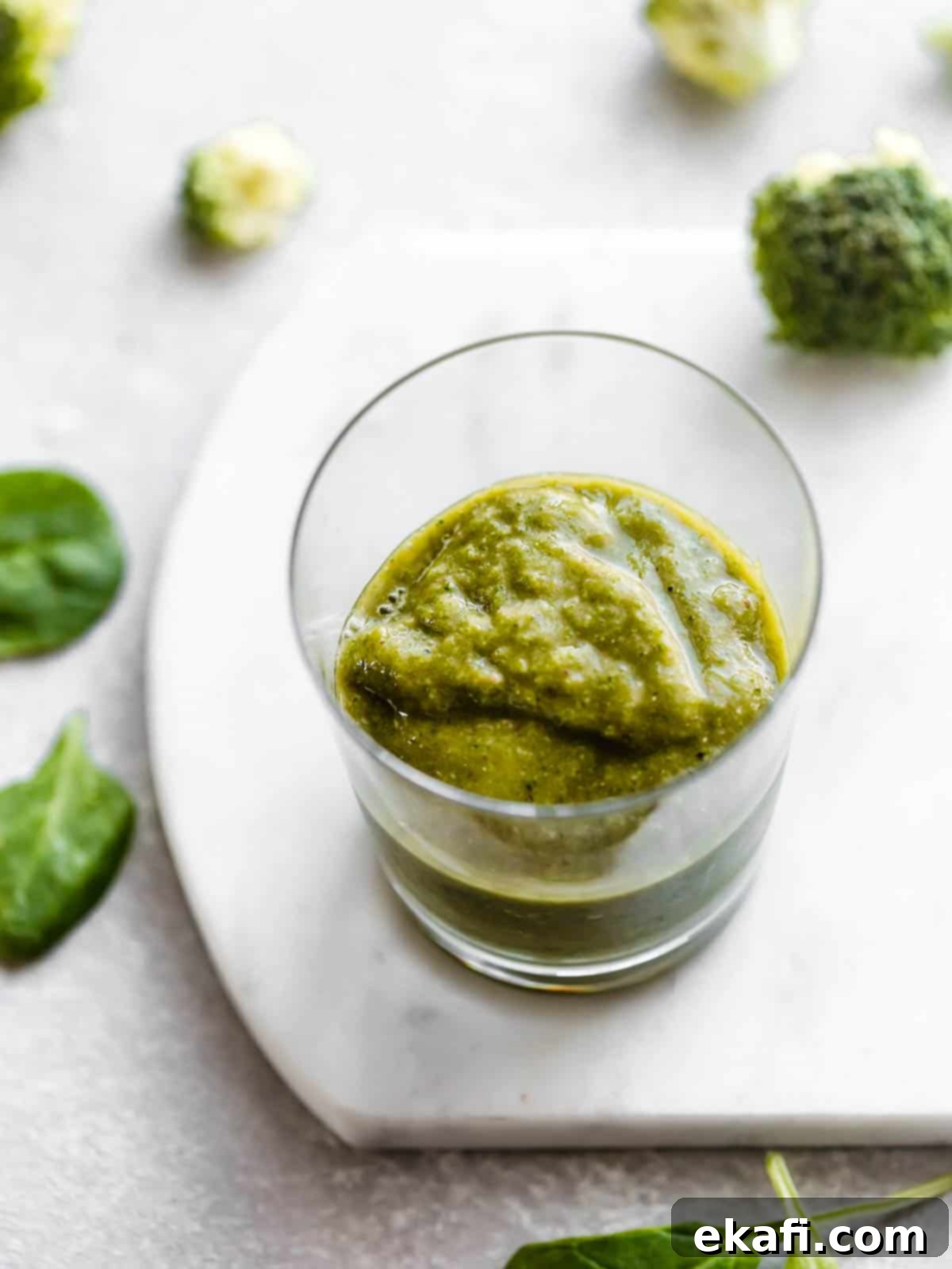 Green Power Smoothie 7 A clear cup half full of Broccoli Smoothie on a white background, showcasing the vibrant green color.