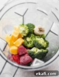 Green Power Smoothie 8 A blender filled with raw broccoli, strawberries, mango chunks, and banana for making a Broccoli Smoothie.