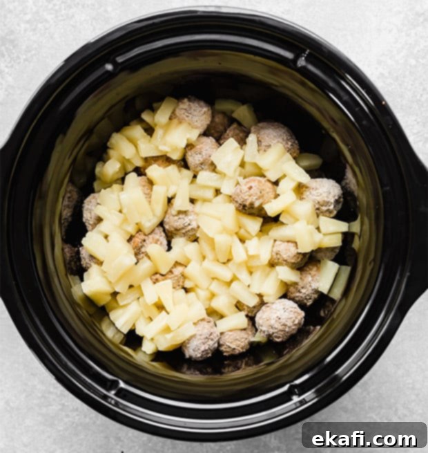 Tangy Sweet Slow Cooker Meatballs 5 A black slow cooker with frozen meatballs and pineapple chunks in it.