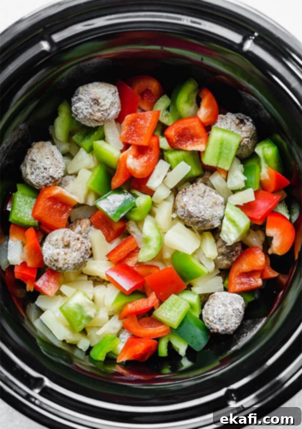 Tangy Sweet Slow Cooker Meatballs 6 A crock pot with frozen meatballs, red and green chopped bell peppers, and pineapple tidbits.