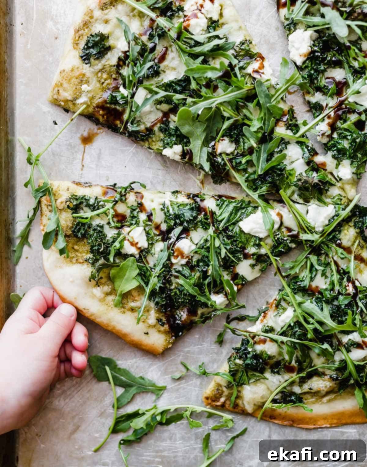 Citadel Pizza 2 A small child's hand reaching for a slice of homemade kale pizza topped with fresh arugula and a rich balsamic glaze, highlighting its irresistible appeal.