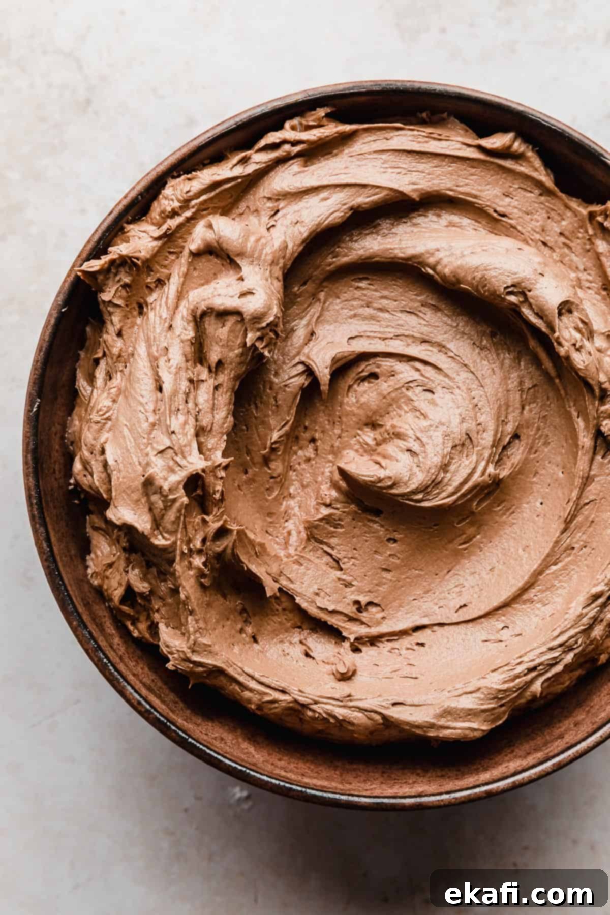 Decadent Chocolate Buttercream 2 A brown bowl full of light brown colored Chocolate Buttercream with Melted Chocolate, showcasing its rich, creamy texture.