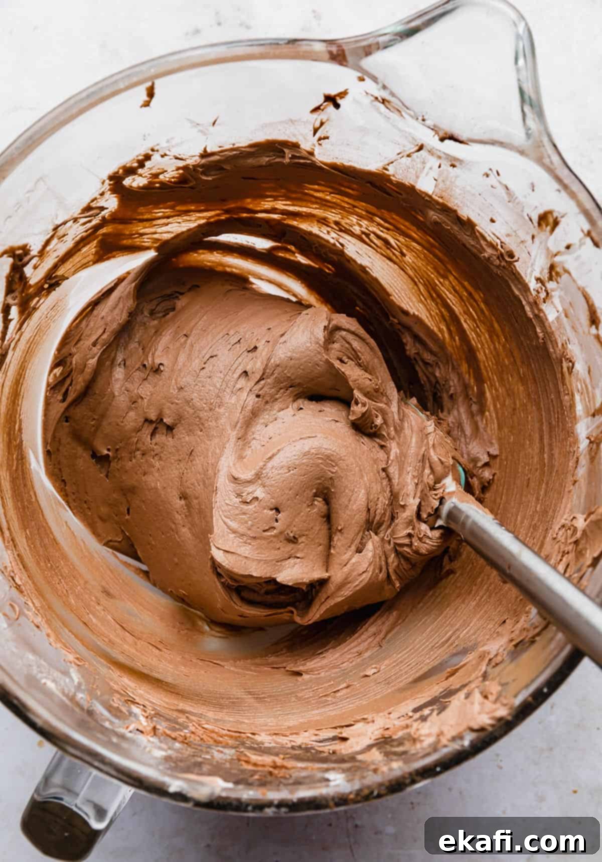 Decadent Chocolate Buttercream 13 A spatula stirring a thick, creamy, and rich chocolate buttercream frosting made with melted chocolate, in a glass bowl.
