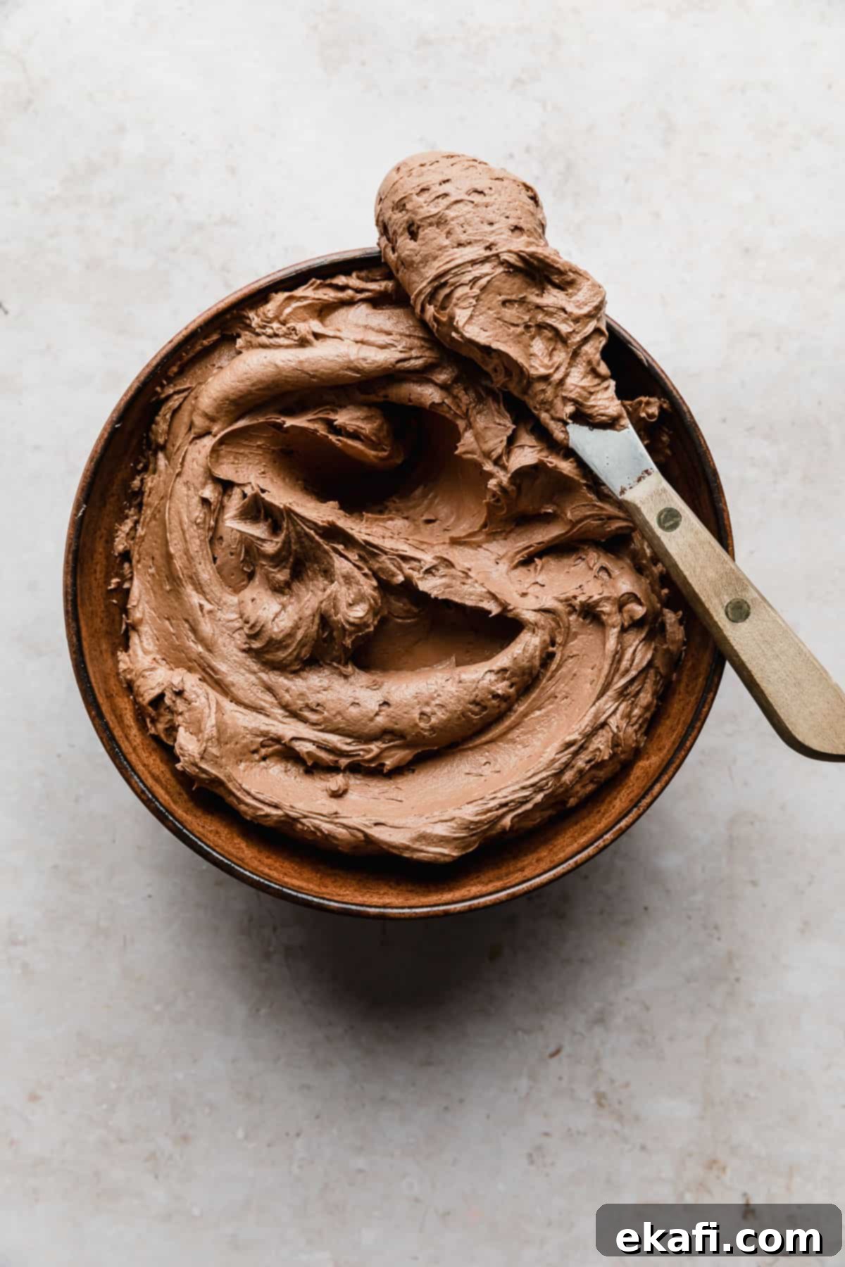 Decadent Chocolate Buttercream 14 Delicious Chocolate Buttercream Frosting Recipe in a brown bowl, perfectly smooth and creamy, set against a cream-textured background.