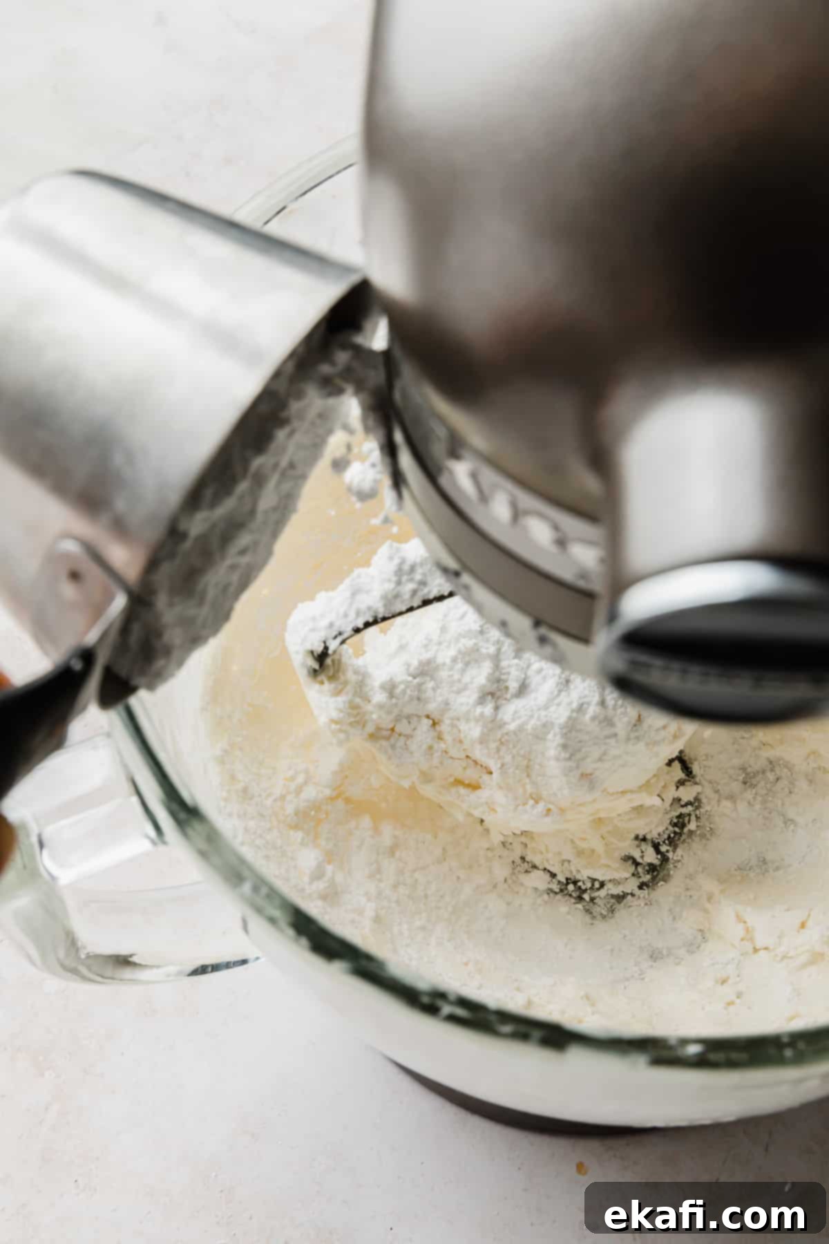 Decadent Chocolate Buttercream 6 Powdered sugar being poured into a stand mixer bowl containing light, creamed butter, to create the Chocolate Buttercream Frosting.