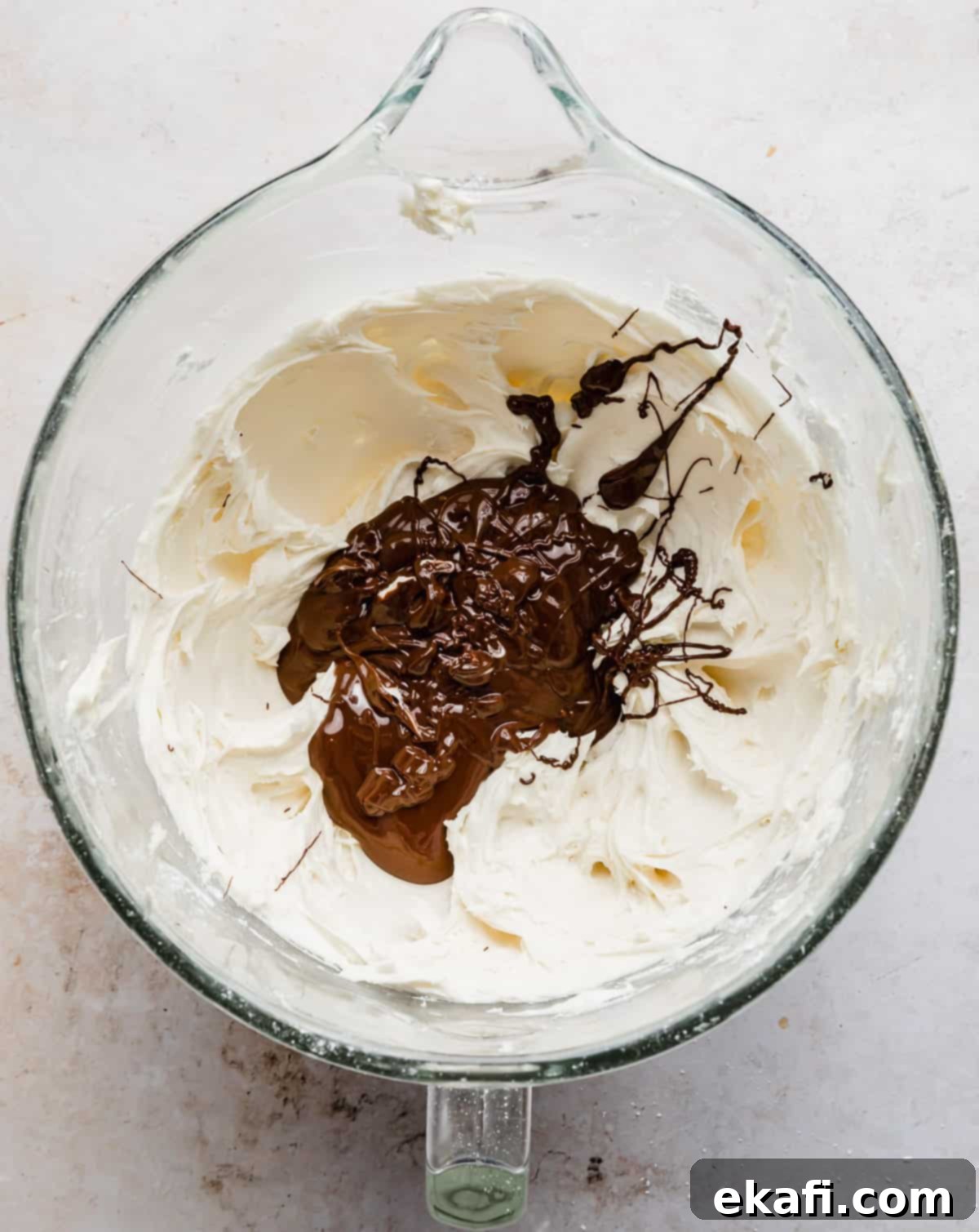 Decadent Chocolate Buttercream 8 Creamed butter and powdered sugar in a stand mixer bowl with melted chocolate being poured overtop, preparing for mixing into the buttercream.