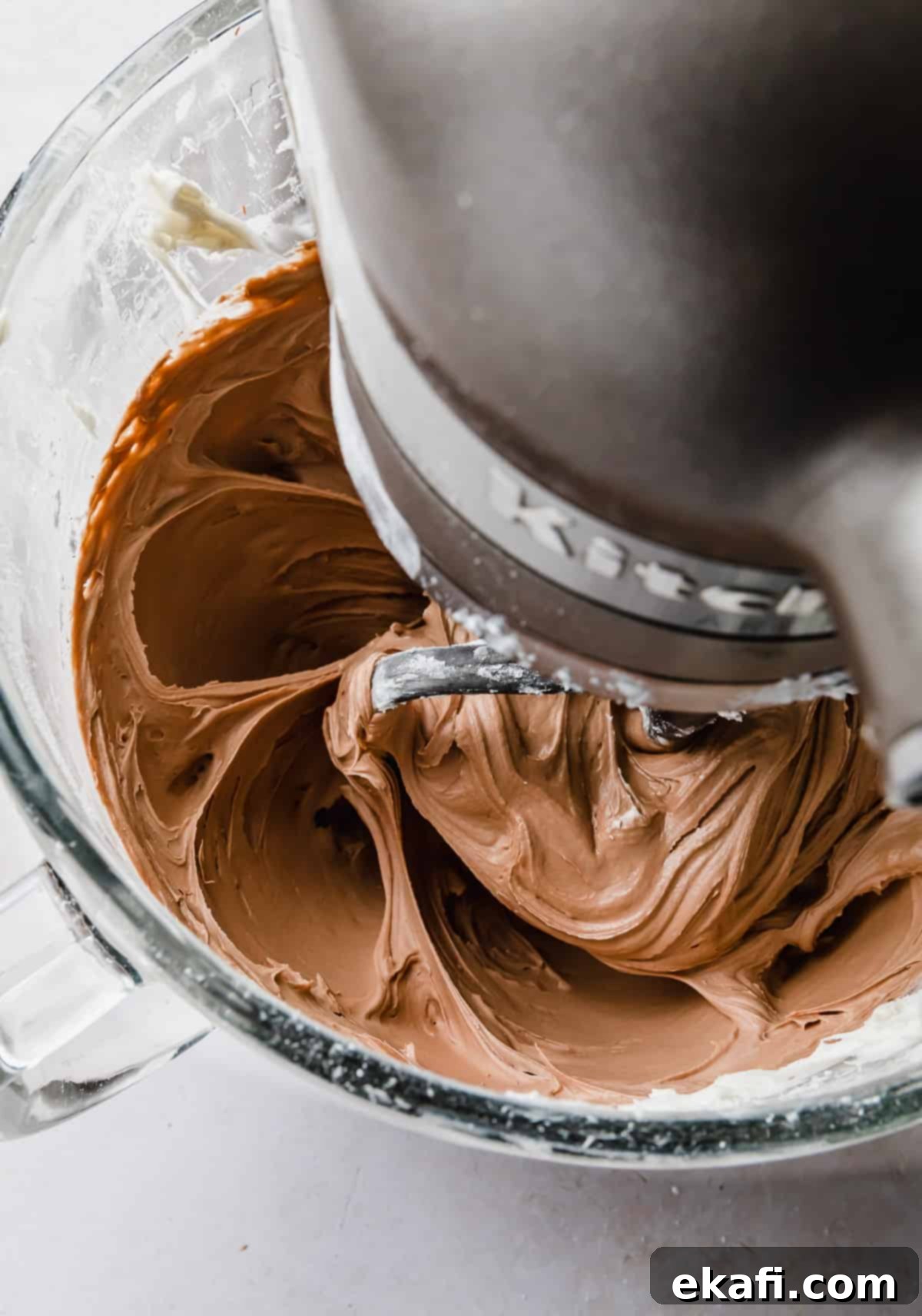 Decadent Chocolate Buttercream 10 Finished Chocolate Buttercream Frosting with Melted Chocolate being stirred in a glass KitchenAid bowl, showcasing its readiness for use.