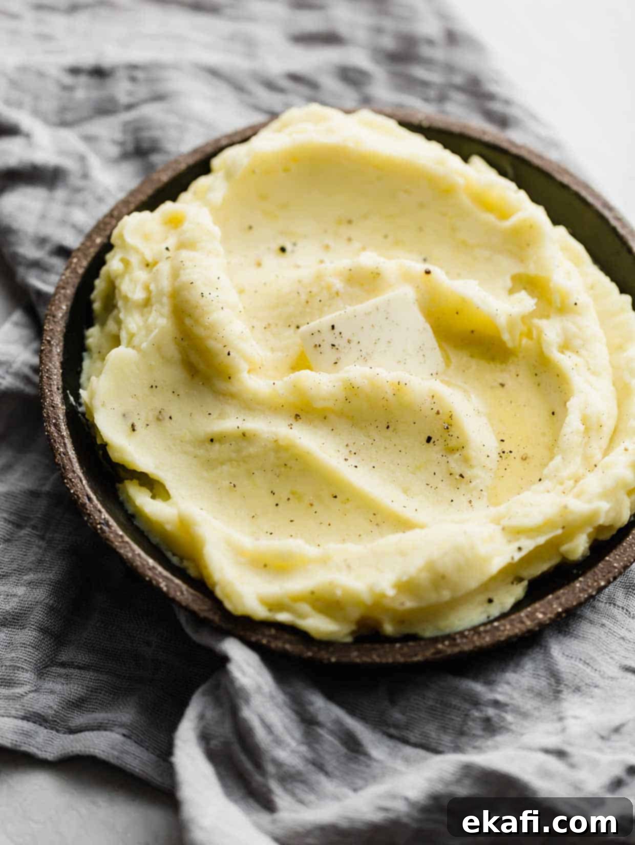 Velvety Half-and-Half Potatoes 5 A slice of butter melting into the top of homemade mashed potatoes on a black plate.
