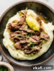 Southern Comfort Mississippi Pot Roast 7 A black plate with mashed potatoes and shredded Mississippi Pot Roast overtop.