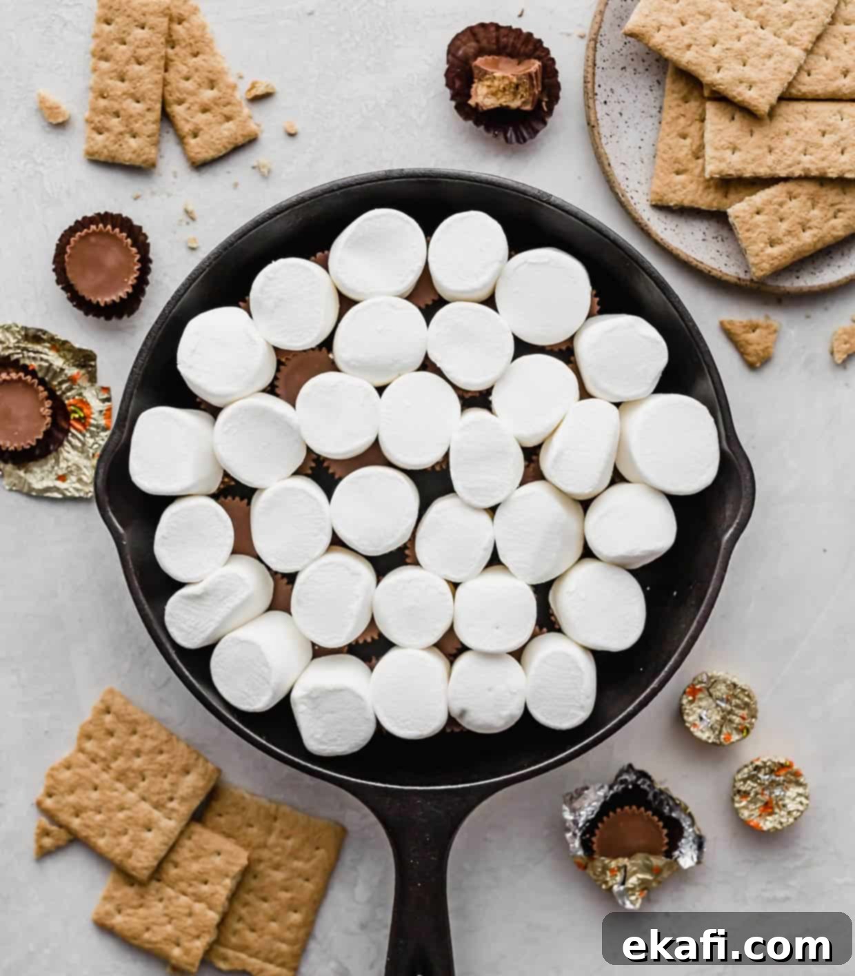 Ντιπ Σμόρες Ρήσης 5 Μεγάλα, αφράτα marshmallows τοποθετημένα πάνω από τα Reese's Peanut Butter Cups σε ένα μαύρο μαντεμένιο τηγάνι, έτοιμα να λιώσουν και να ροδίσουν.