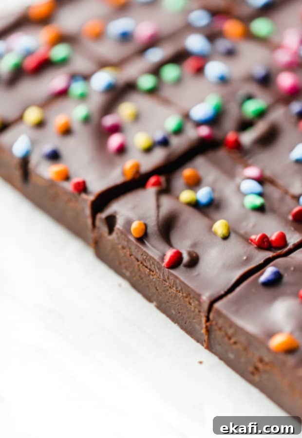 Stardust Brownies 16 Several perfectly cut Cosmic Brownies with shiny ganache and colorful chips, displayed on white parchment paper.