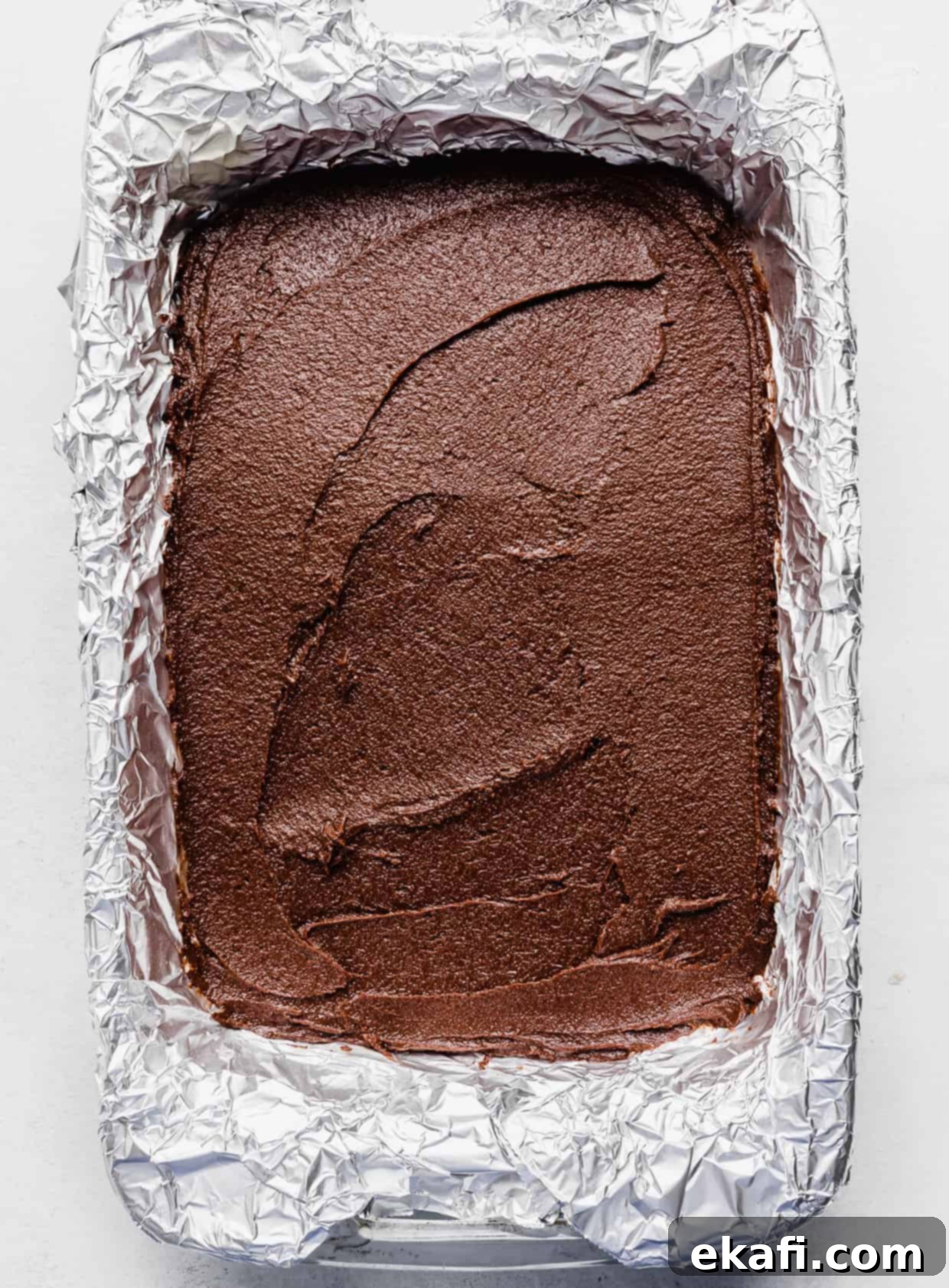 Stardust Brownies 10 An aluminum foil lined baking dish filled with thick, unbaked Cosmic Brownie batter, leveled smooth.