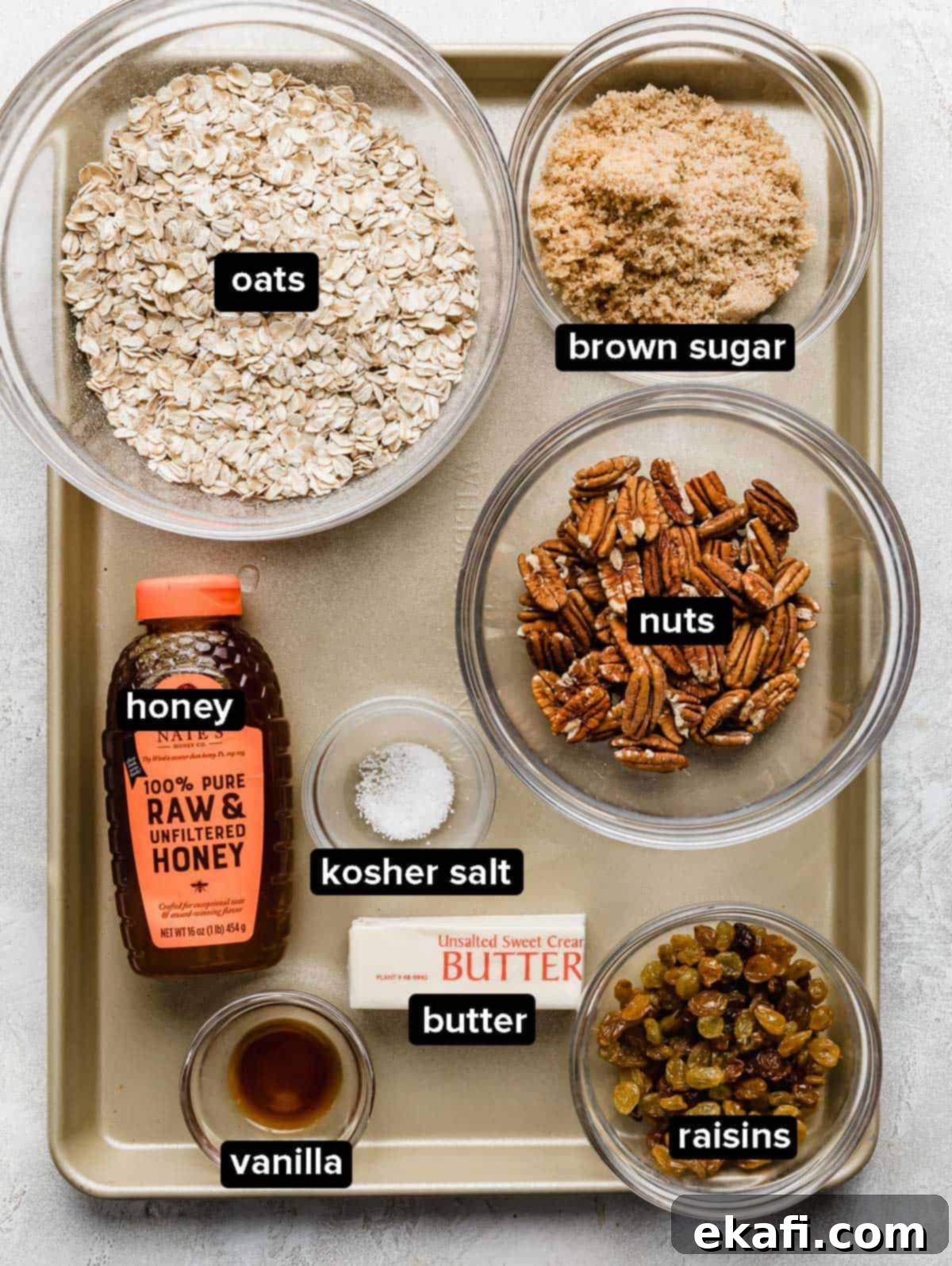 Μπάρες Γκρανόλα Βρώμης Σταφίδας 3 Homemade granola bar ingredients in glass bowls on a bronze colored baking sheet.