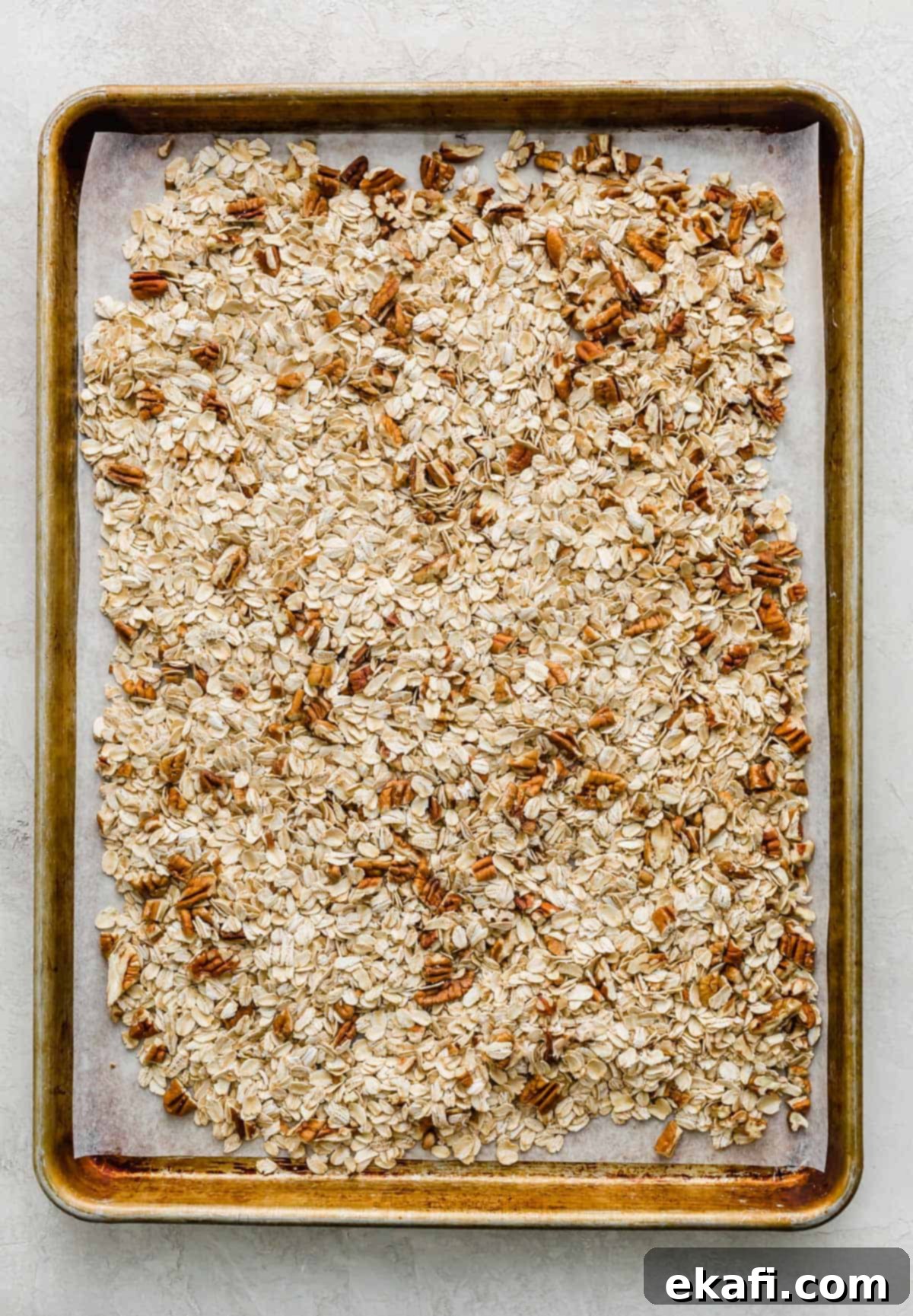Μπάρες Γκρανόλα Βρώμης Σταφίδας 4 A baking sheet with old fashioned oats and chopped pecans spread across the surface of it.