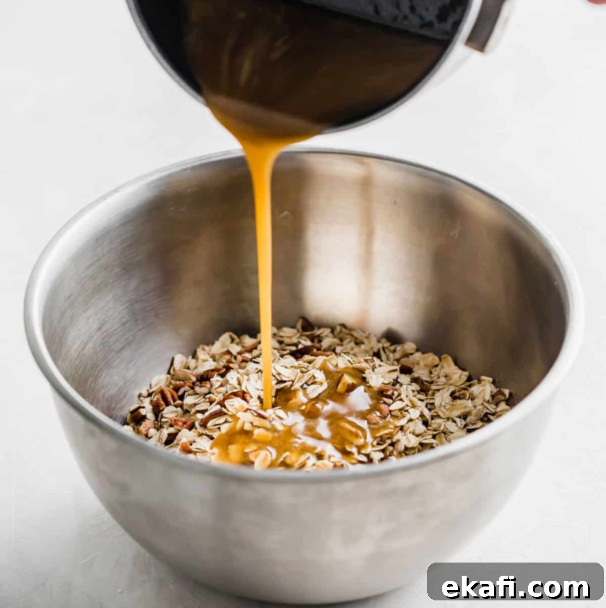 Μπάρες Γκρανόλα Βρώμης Σταφίδας 5 A brown liquid being poured from a small pot into a metal bowl filled with Oatmeal Raisin Granola Bar mixture.